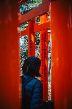 A visitor explores the iconic red torii gates at Fushimi Inari Shrine, Kyoto, Japan, surrounded by nature.