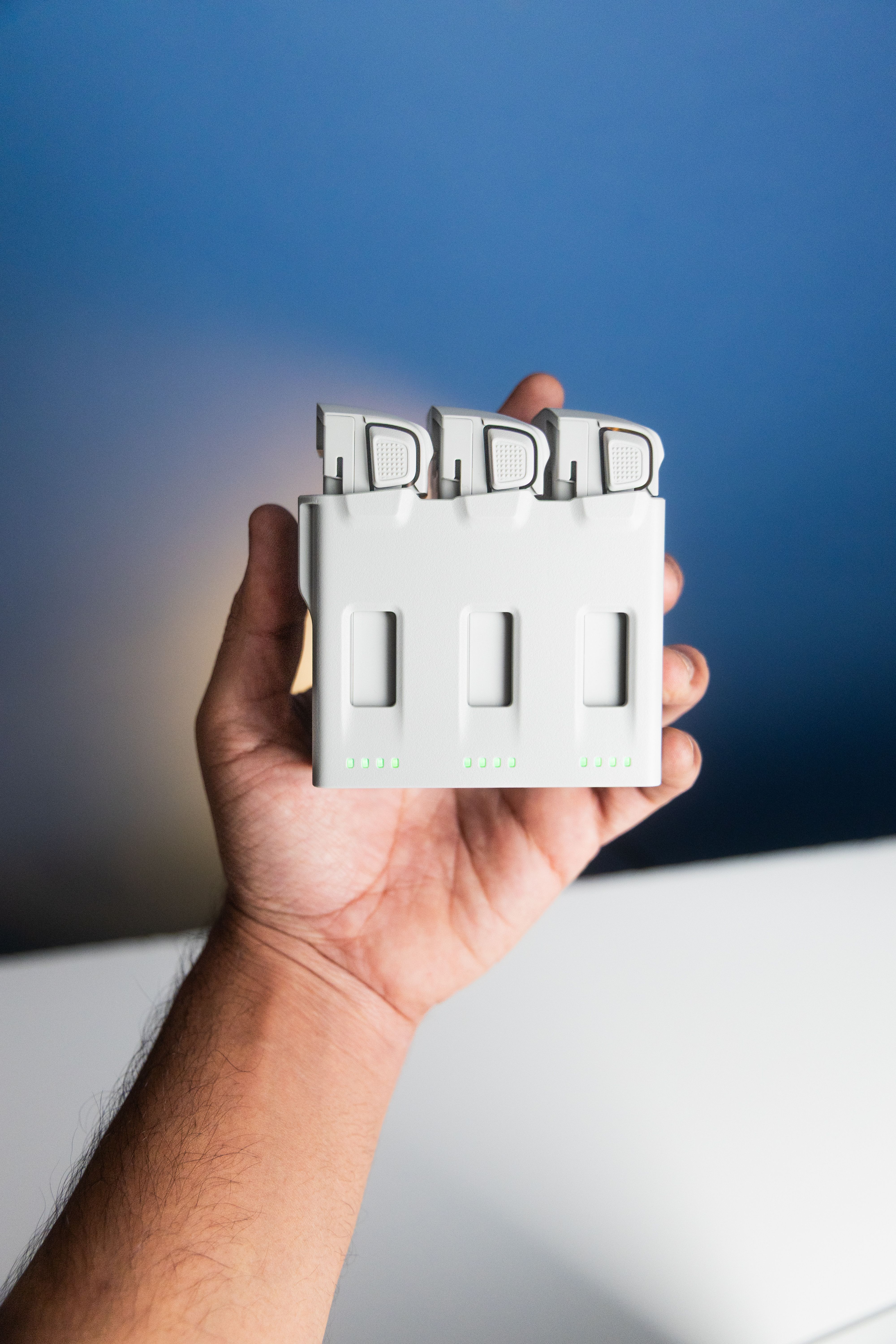 Close-up of a hand holding a drone battery charger indoors with a blue background.