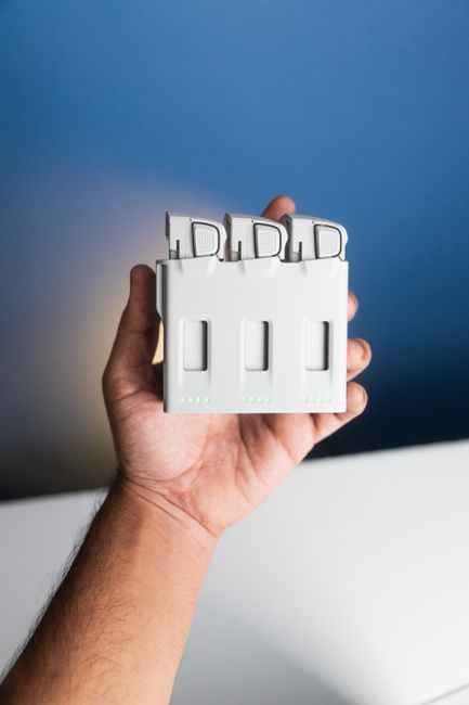 Close-up of a hand holding a drone battery charger indoors with a blue background.