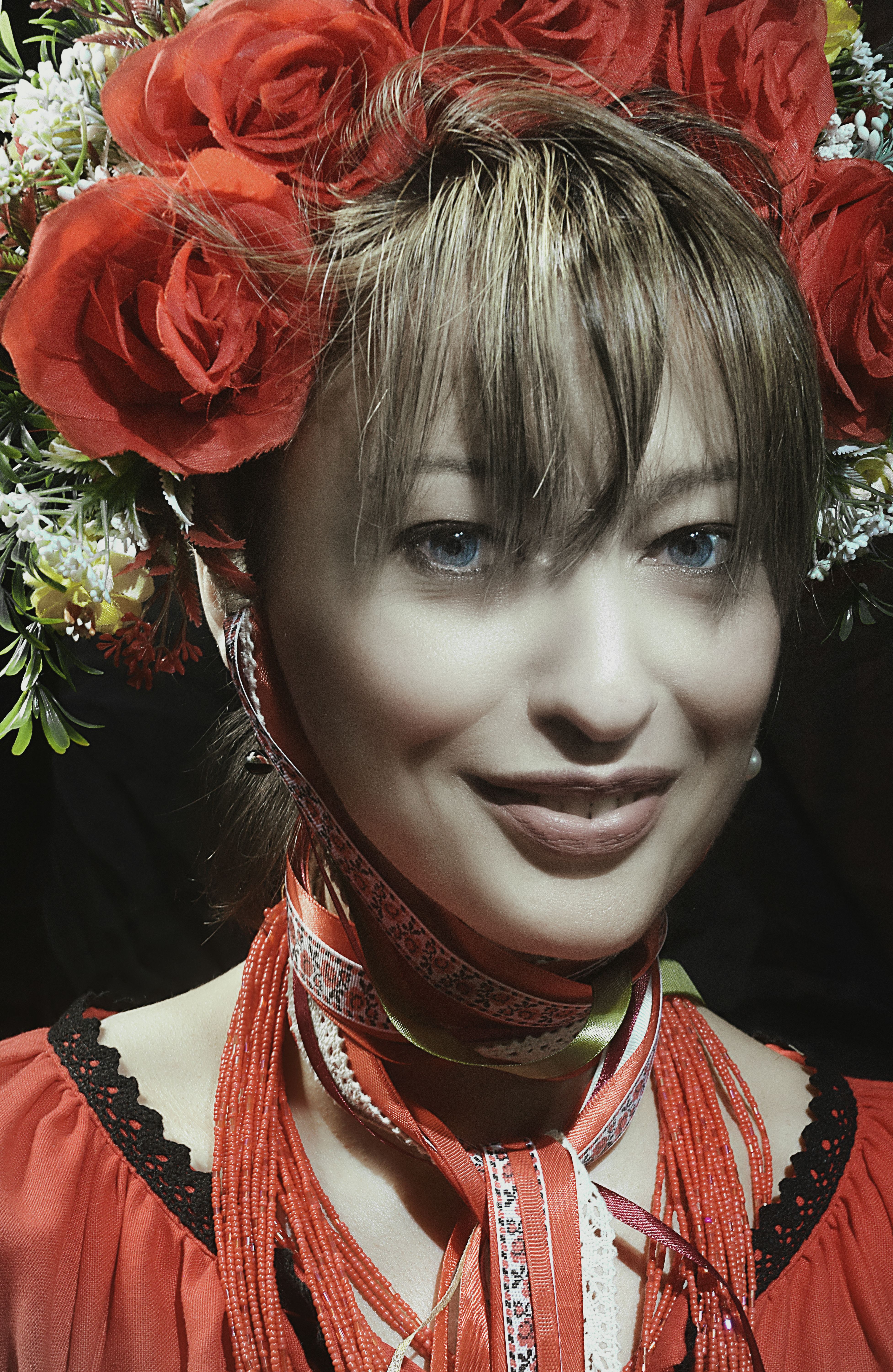 Woman in ethnic attire with vibrant red floral headpiece, smiling.