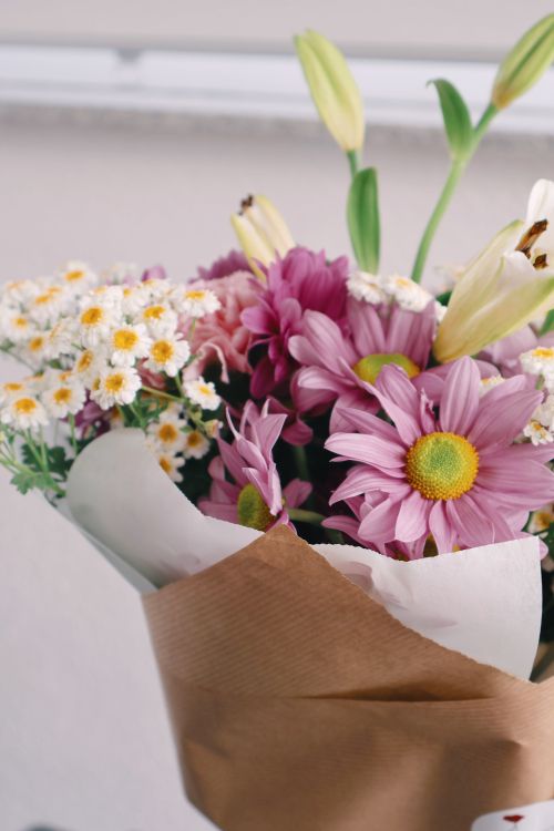 Free A vibrant bouquet featuring daisies and lilies wrapped in brown paper. Stock Photo