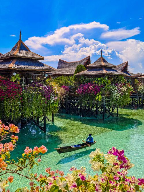 Free Traditional Asian water villa with vibrant bougainvillea overlooking a clear turquoise lagoon. Stock Photo