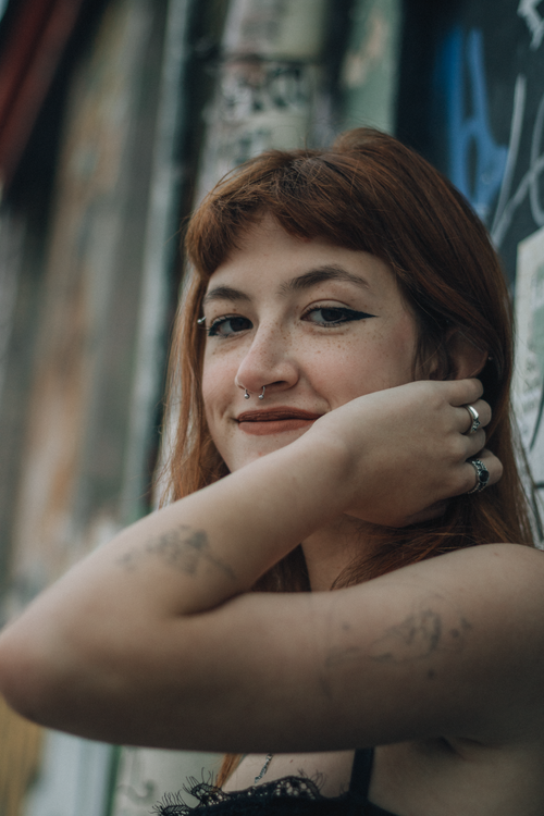 Free Portrait of a young woman with tattoos in front of a graffiti-covered wall, exuding artistic urban vibe. Stock Photo