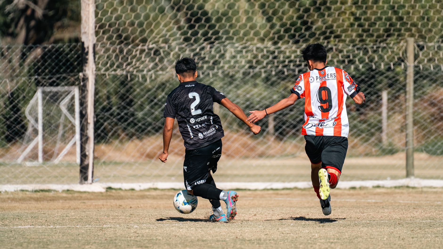 Two young soccer players in action during a daytime outdoor match on a grassy field.
