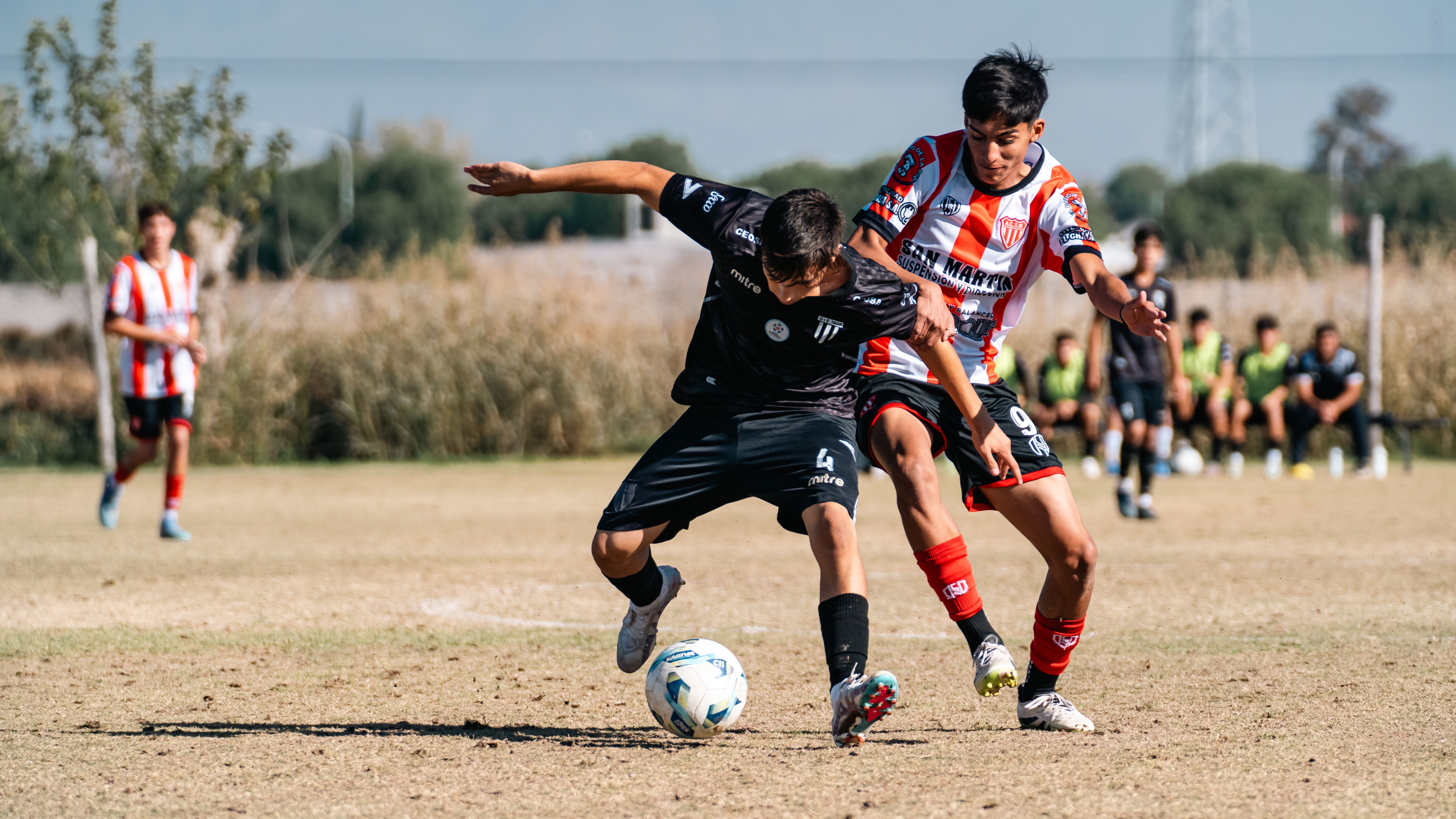 Young soccer players competing fiercely during a sunny day match on an outdoor field.