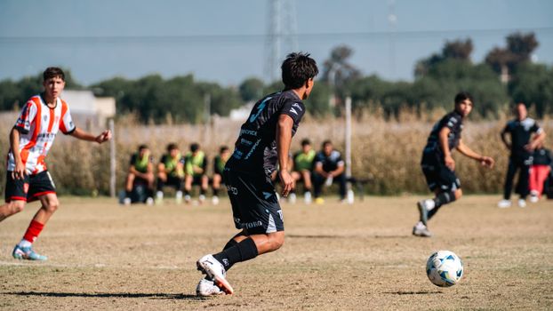 Teenagers compete in an outdoor soccer match, with players in action and a sunny day backdrop.