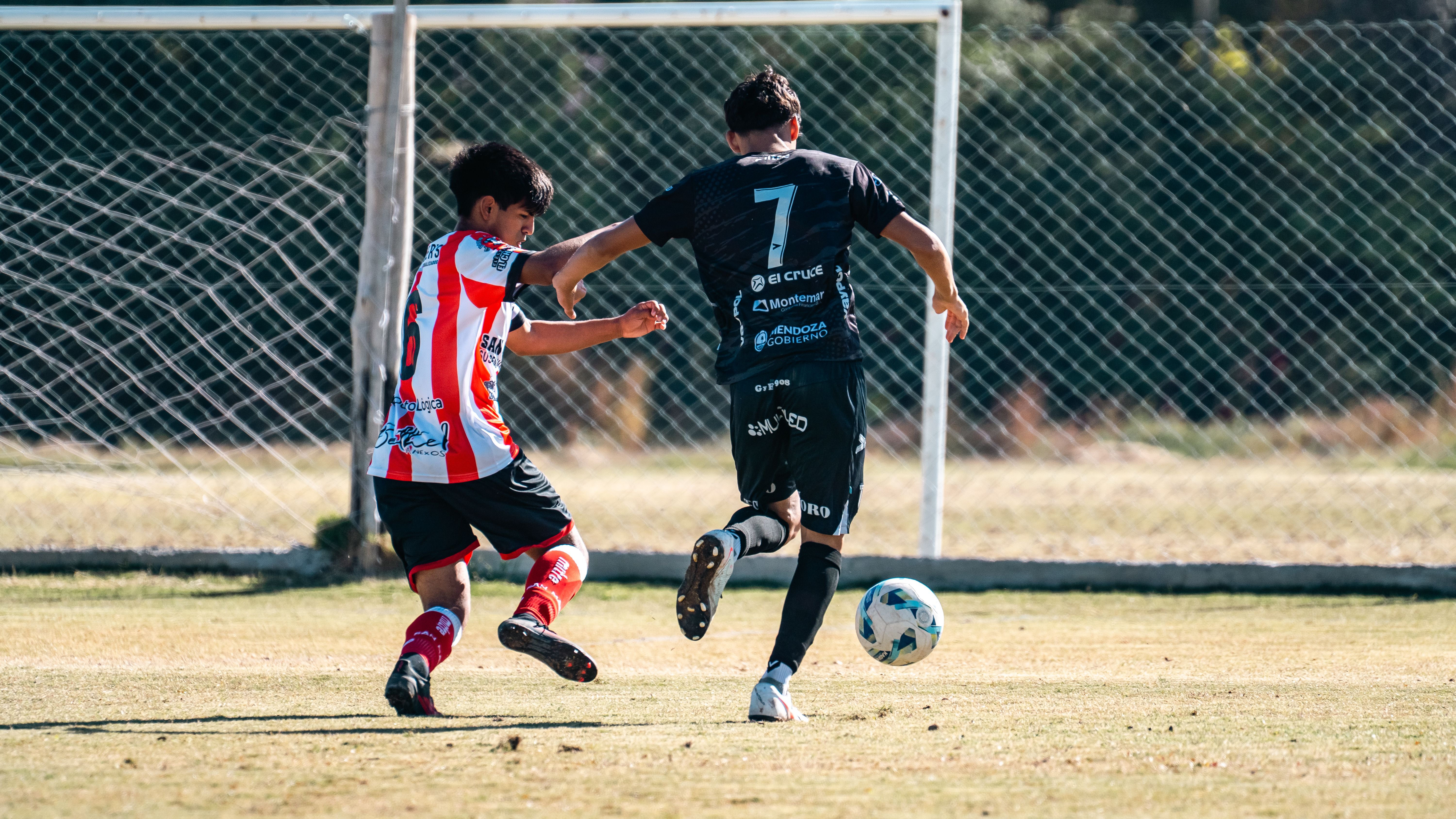 Two young soccer players compete during an intense match on a sunny day.