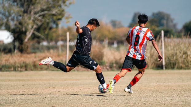Two soccer players in action during a game on an open field under clear skies.