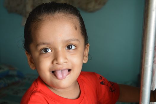 A happy child playfully sticking out their tongue indoors, capturing joyful innocence.