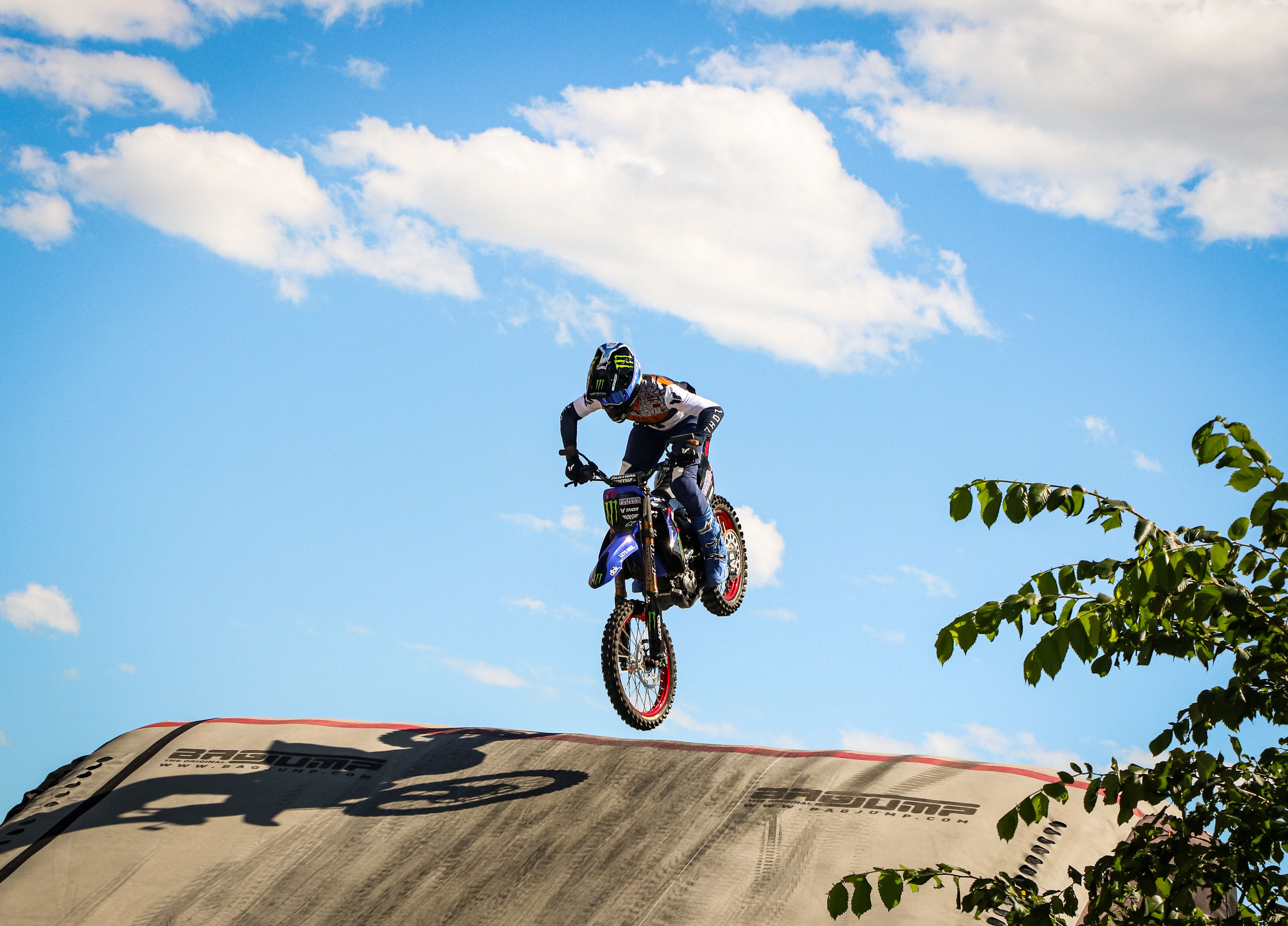 Dramatic image of a motocross rider performing a jump against a bright blue sky with clouds.
