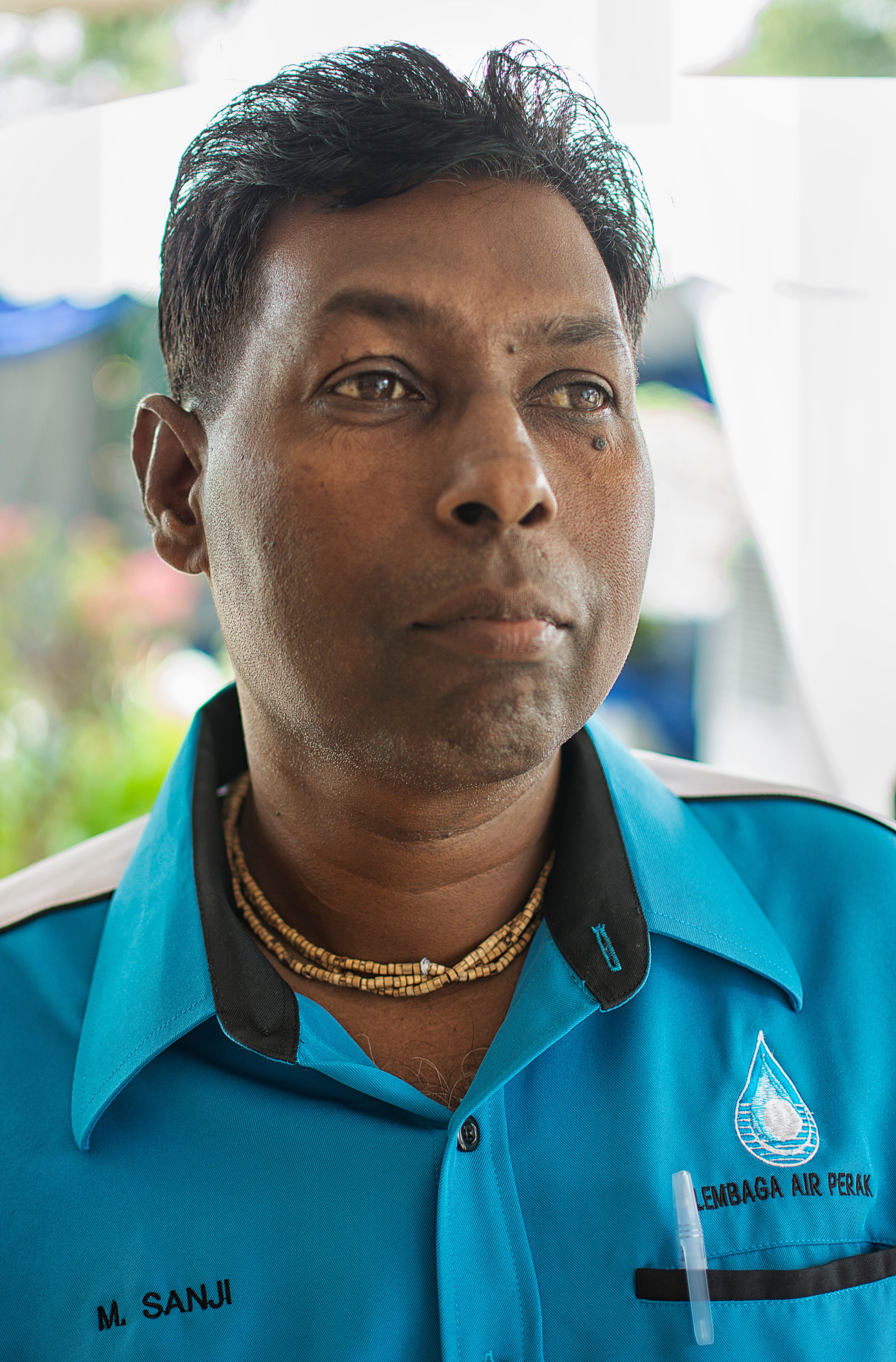 Close-up portrait of a man in a blue uniform appearing thoughtful outdoors.