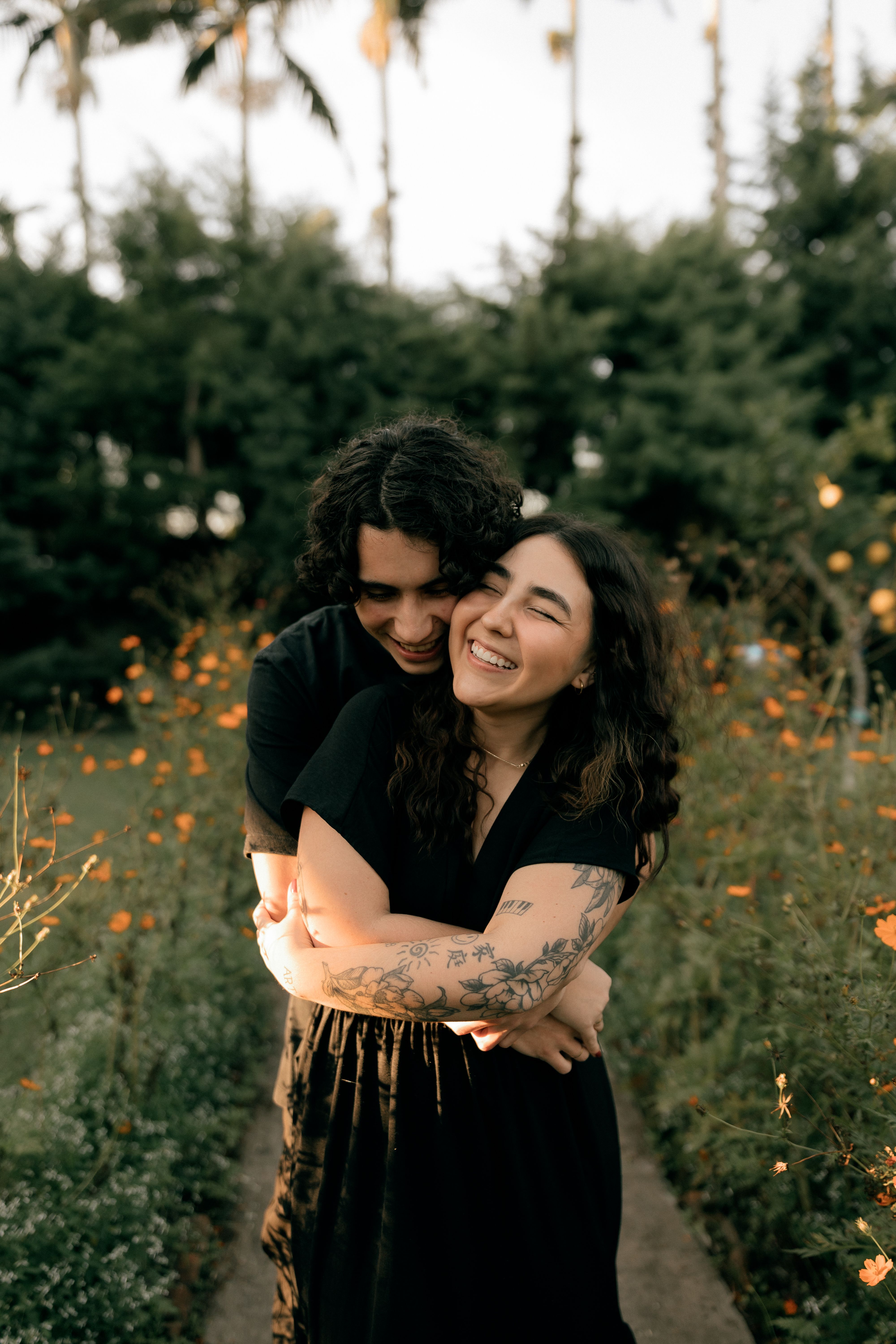 Smiling couple embracing in a garden surrounded by greenery and flowers, conveying joy and love.