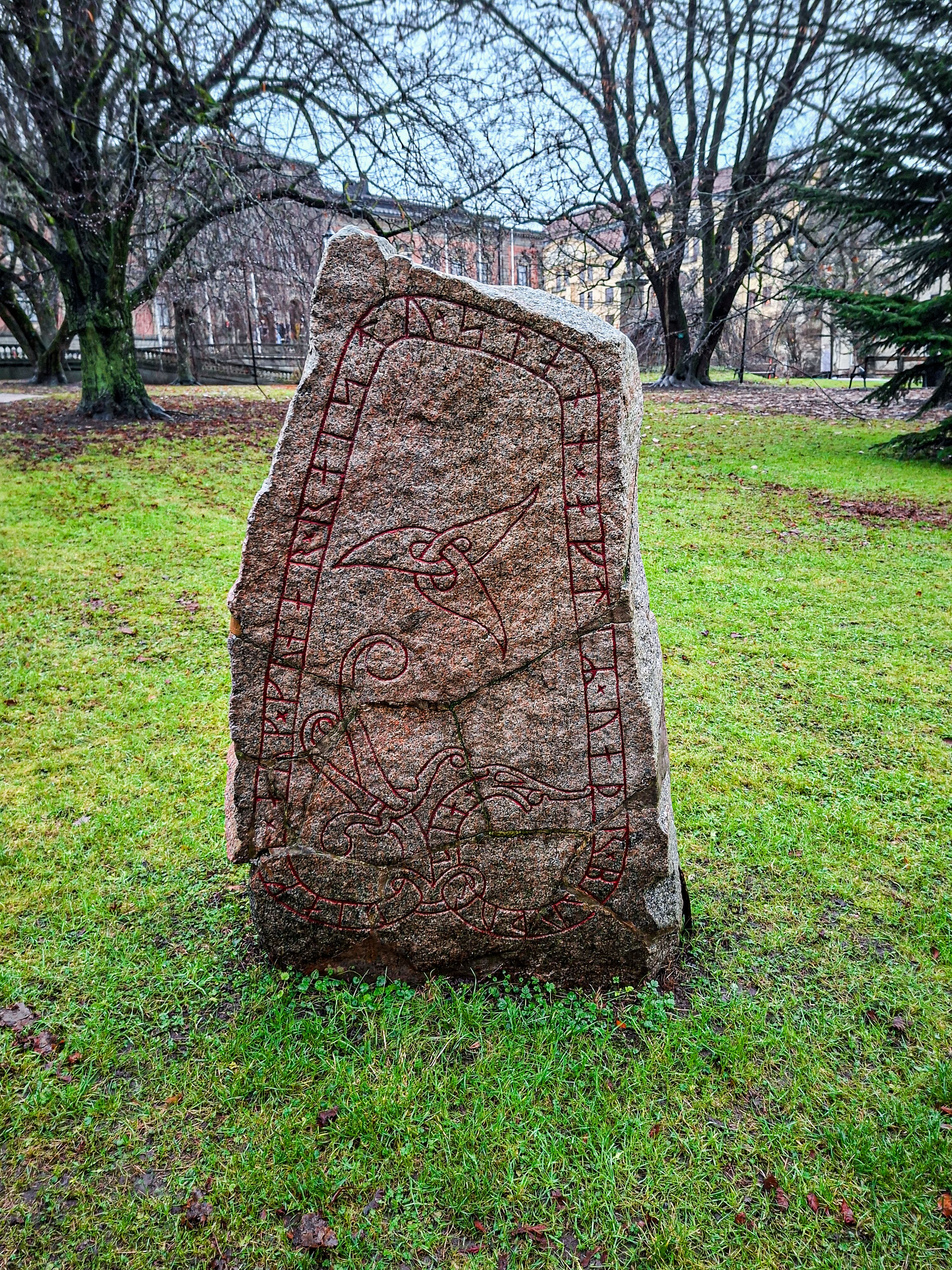 Ancient runestone with Norse engravings standing in a lush green park in Uppsala, Sweden.