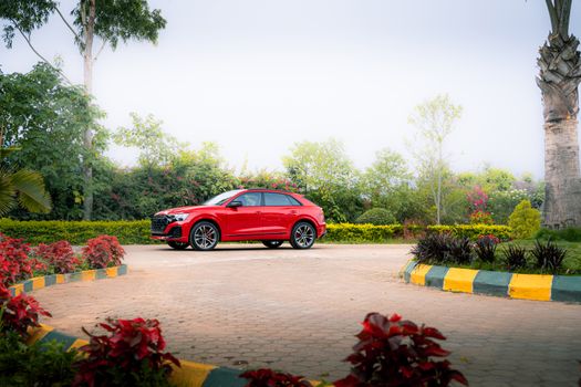 A vibrant red luxury car parked in a picturesque outdoor setting with lush greenery.