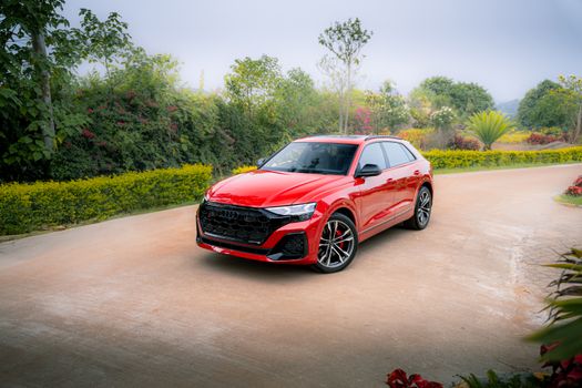 A vibrant red car parked on a scenic road surrounded by lush greenery.
