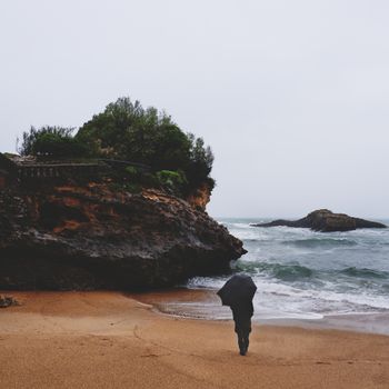 A person with an umbrella walks along a rainy beach in Biarritz, France.