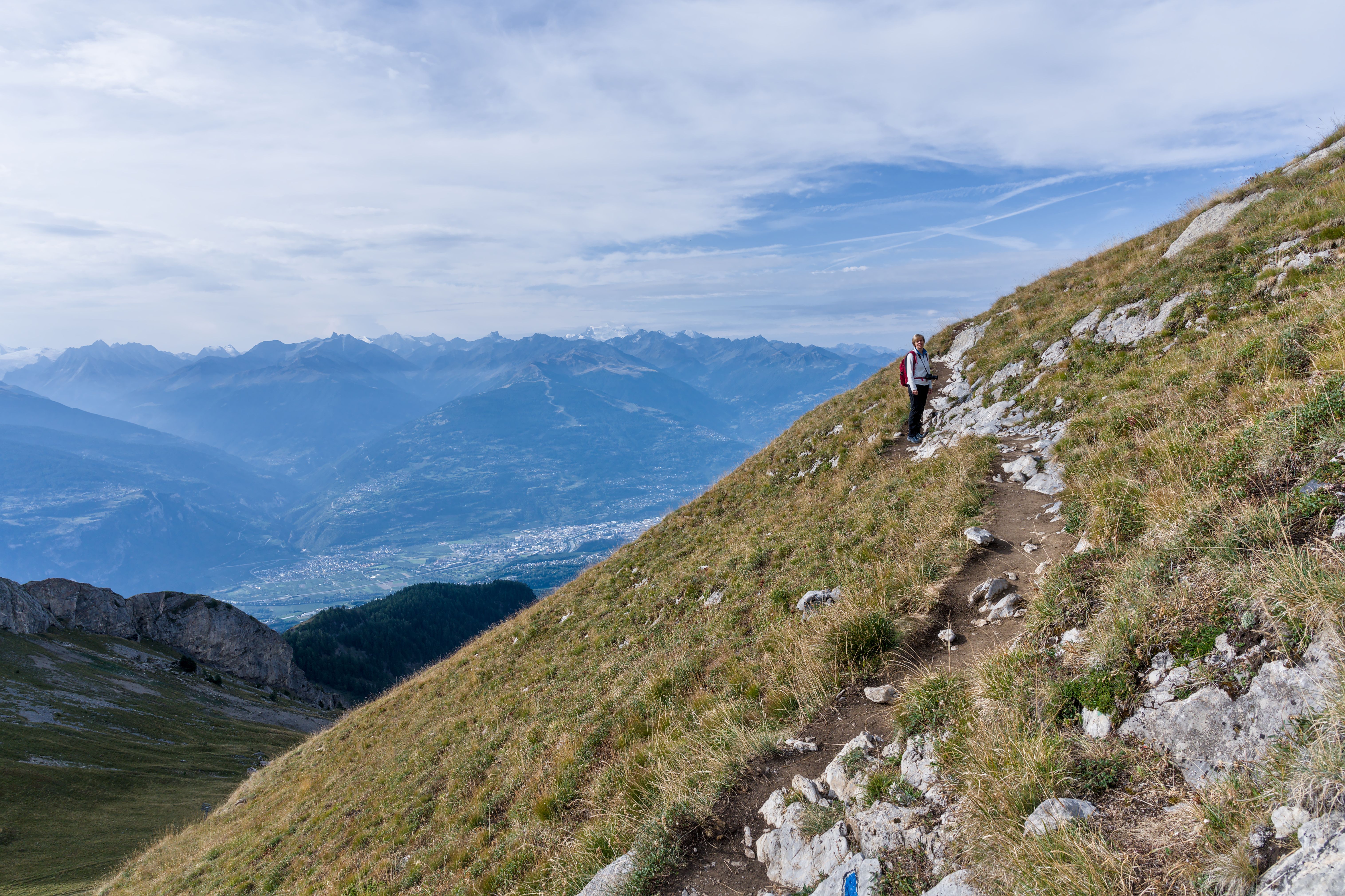 hiker with a small backpack looking at a panoramic view from a mountain path