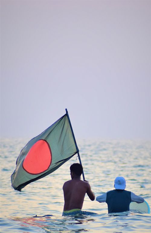 Free Two people in the sea holding the Bangladesh flag at sunset in Cox's Bazar. Stock Photo