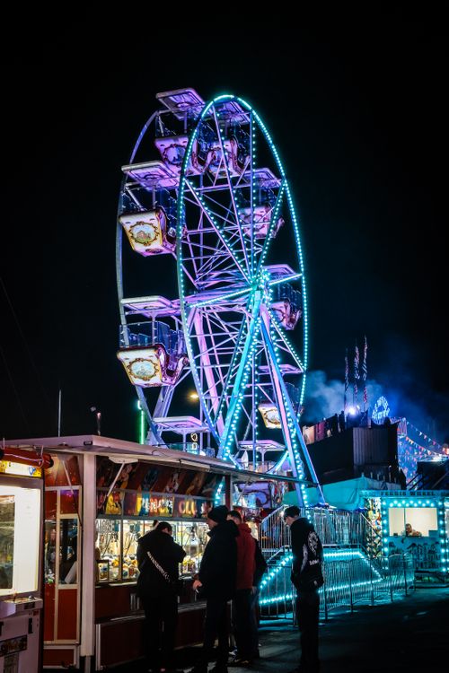 Free Illuminated ferris wheel at a lively night carnival with people enjoying the scene. Stock Photo