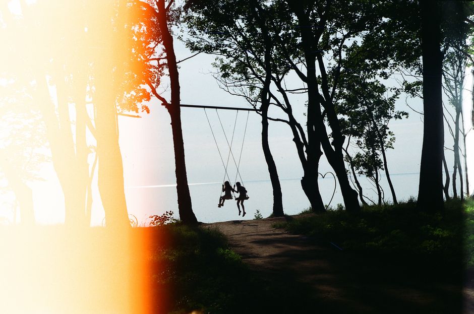 Children swinging among trees at sunrise, silhouetted against the light in Kaliningrad.