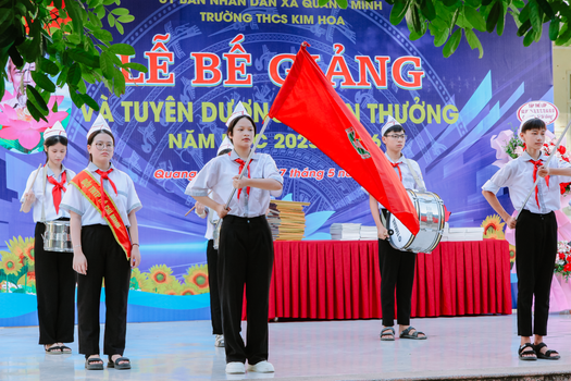 Students performing at a school closing ceremony with musical instruments and flag.