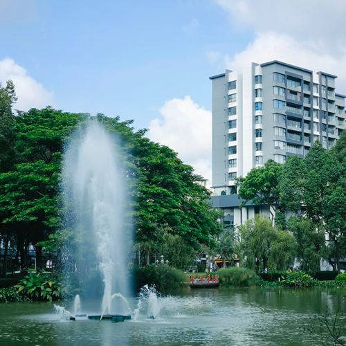 Free Urban park scene featuring a large fountain and modern residential building in daylight. Stock Photo