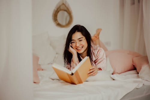 Woman in Pink Long Sleeve Shirt Holding Brown Book