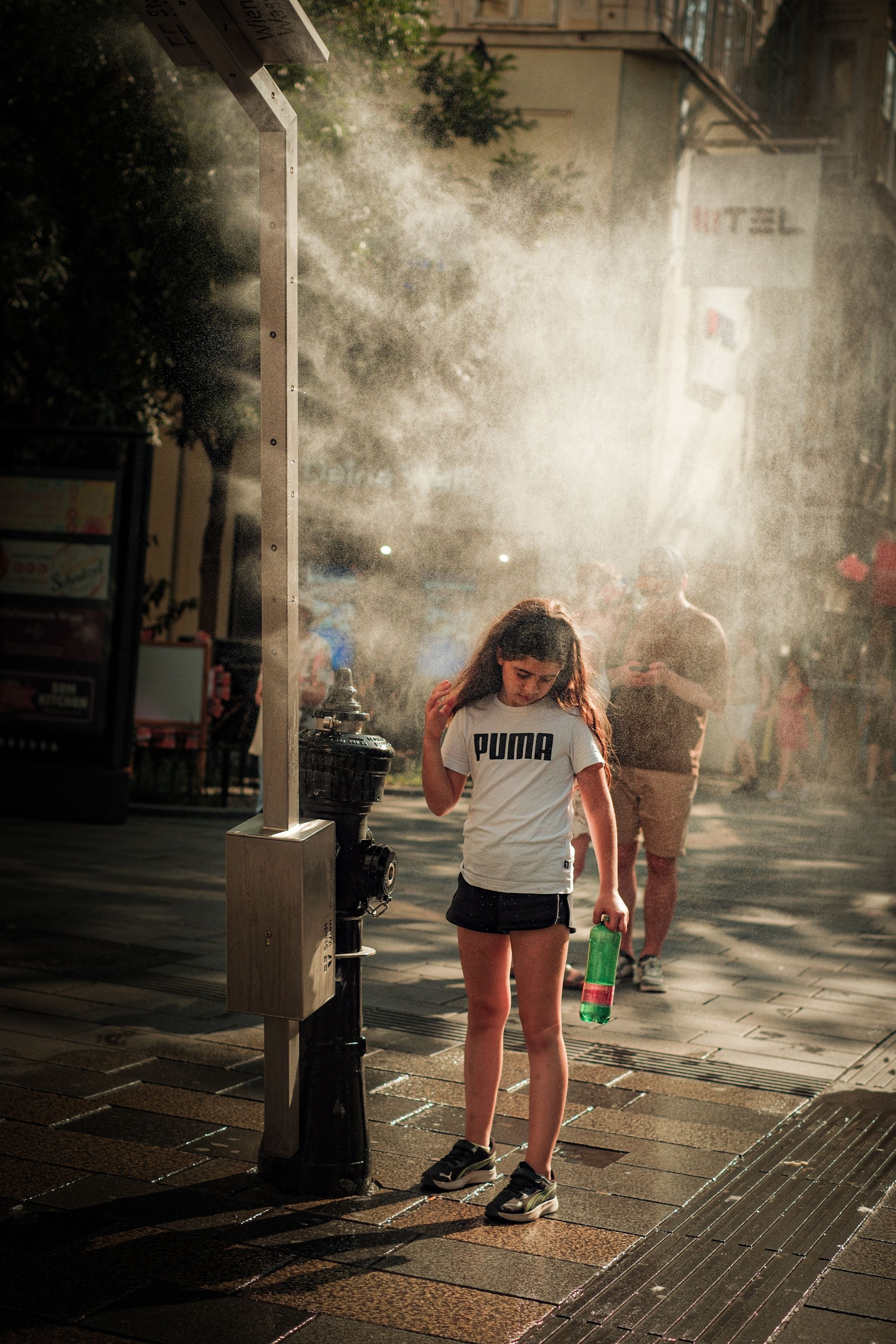 Person cooling off under an outdoor misting fan on a sunny day