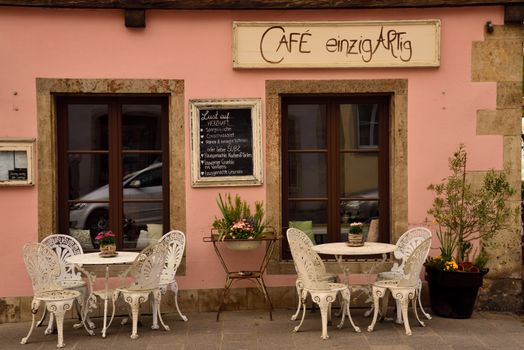 Picturesque outdoor café in Rothenburg ob der Tauber with vintage chairs and a pink wall.