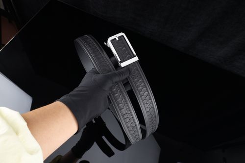 Free Black leather belt held by gloved hand, showcasing elegant silver buckle detail. Stock Photo