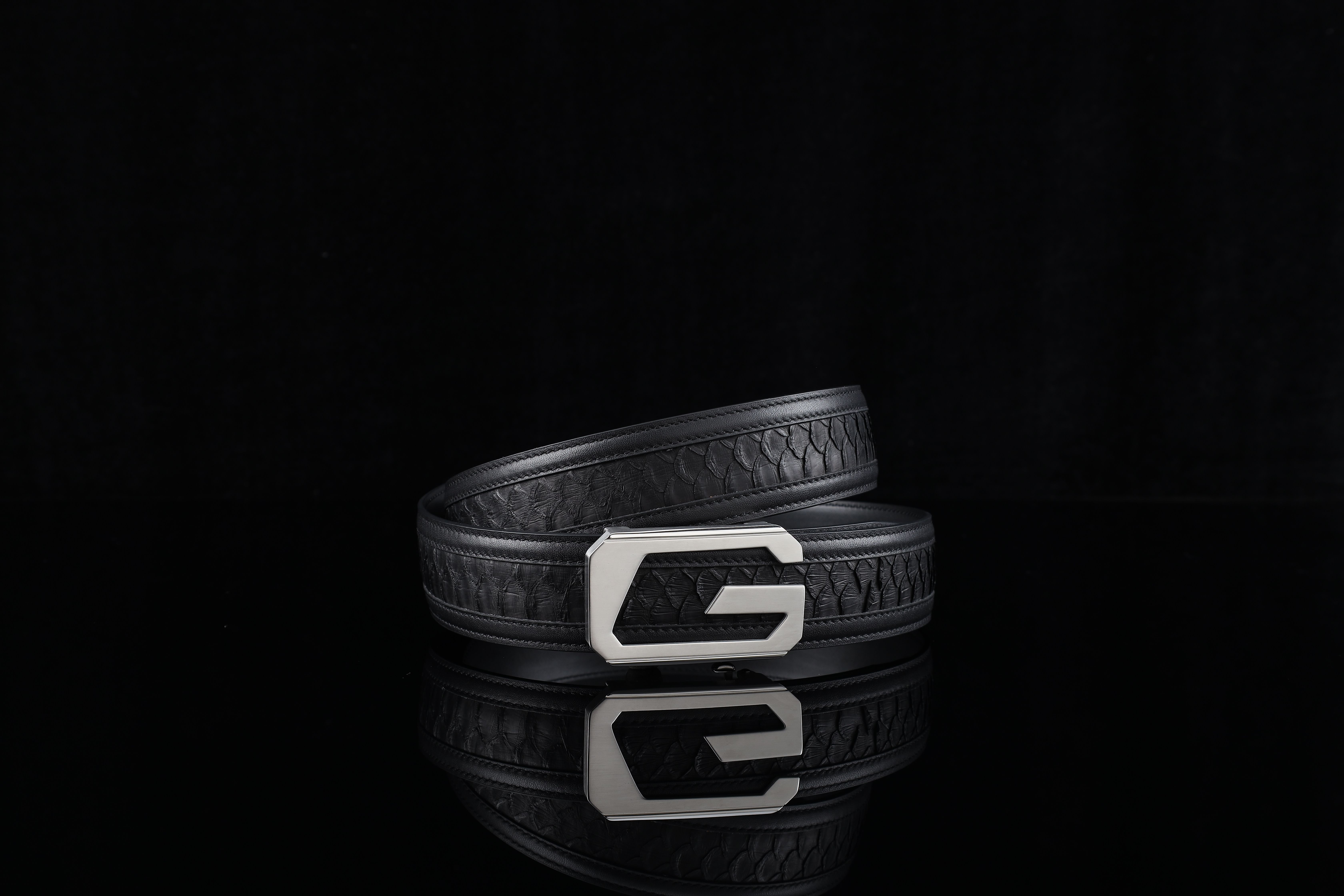 A stylish black leather belt with a distinctive silver buckle on a reflective black surface.