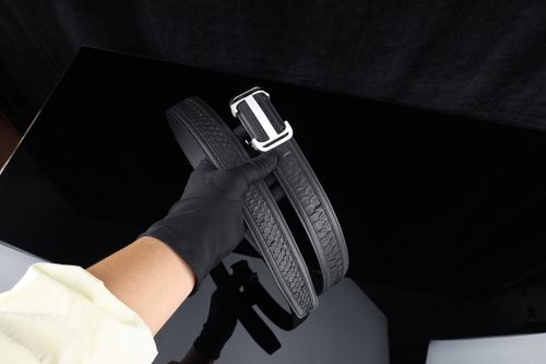 Free Close-up of a gloved hand holding a luxury black leather belt on a black background. Stock Photo