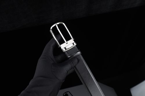 Free Close-up of a stylish black leather belt with a shiny silver buckle, held in a gloved hand. Stock Photo