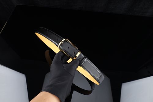 Free Elegant black leather belt with gold buckle held by gloved hand in studio. Stock Photo