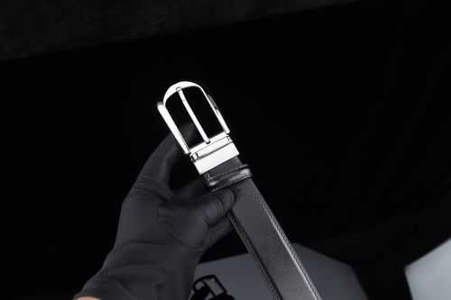 Free A stylish black leather belt with a silver buckle held by a gloved hand against a dark background. Stock Photo