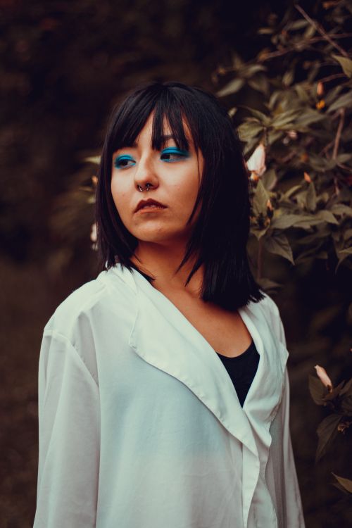 Free A woman with blue eye makeup and a nose ring stands pensively outdoors in a white shirt. Stock Photo
