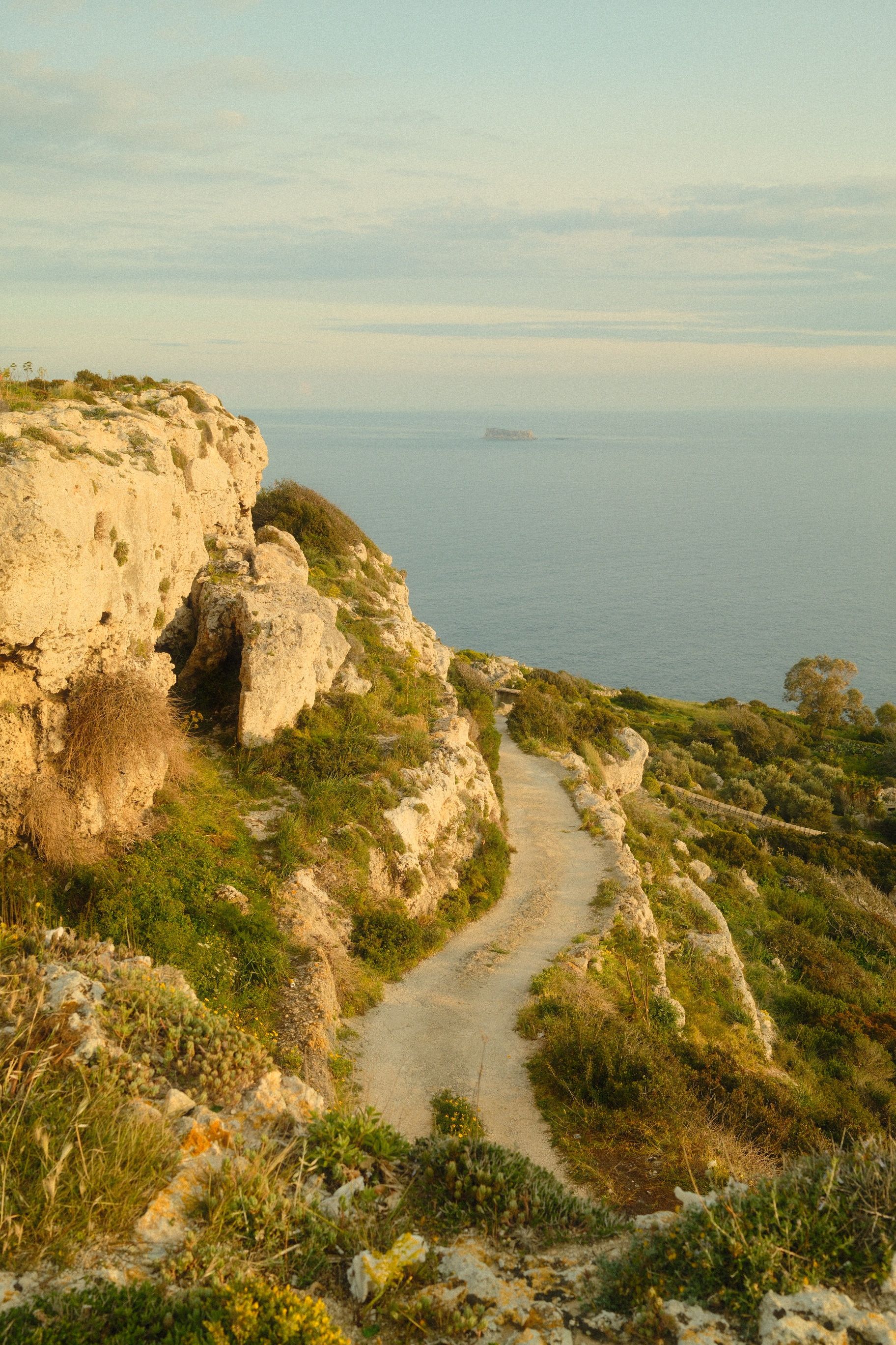 A serene coastal path surrounded by cliffs and ocean views in Malta during the golden hour.