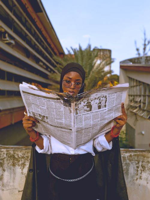 Free A young woman reads a newspaper outdoors in Zaria, Nigeria, blending focus and style. Stock Photo
