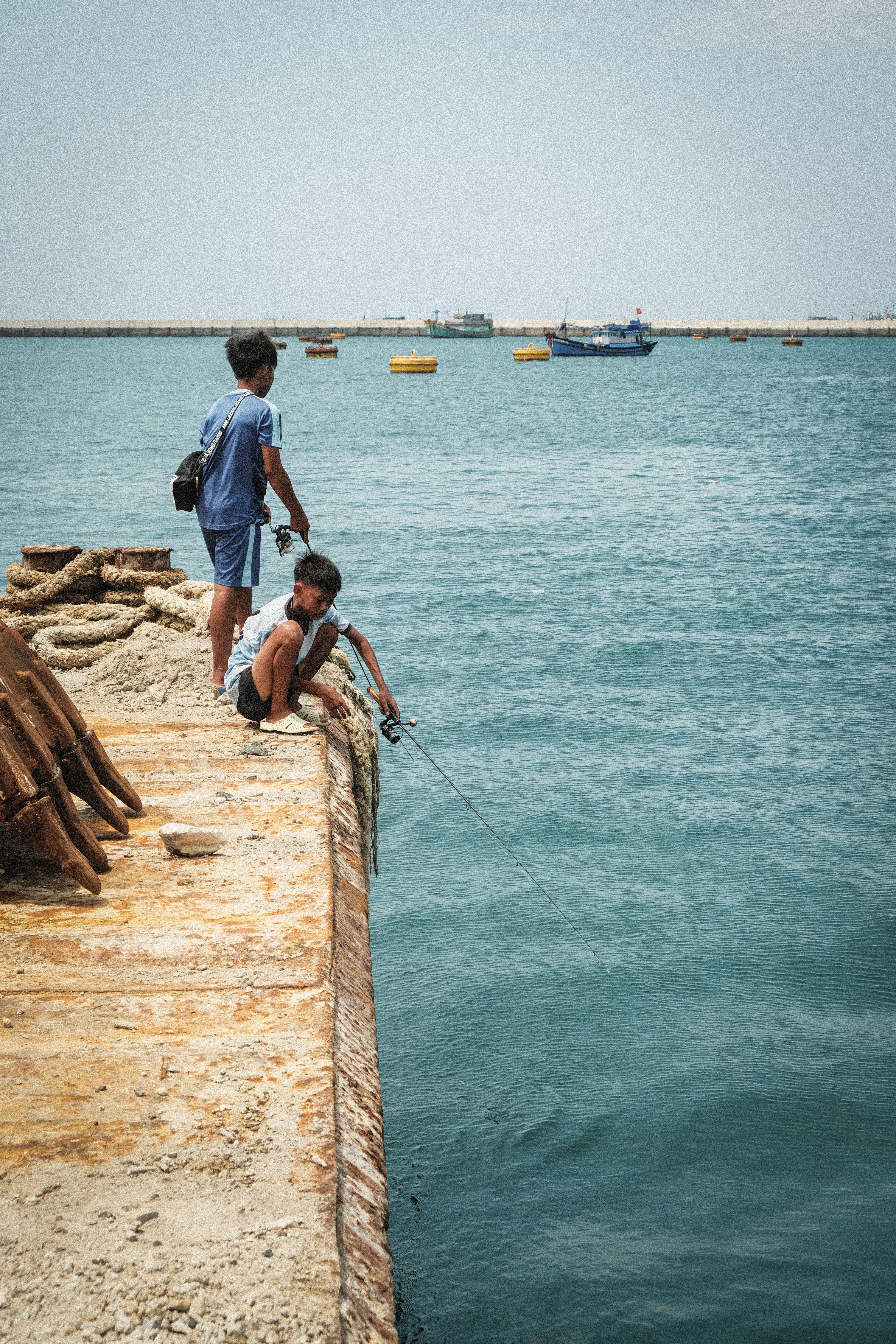 Two boys fishing from a pier in a tranquil sea setting.