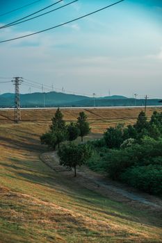 Serene landscape with hills, power lines and trees under a clear day sky.