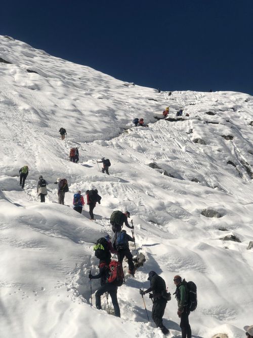 Free Group of trekkers ascending a snowy Himalayan trail under a clear blue sky, showcasing adventure. Stock Photo