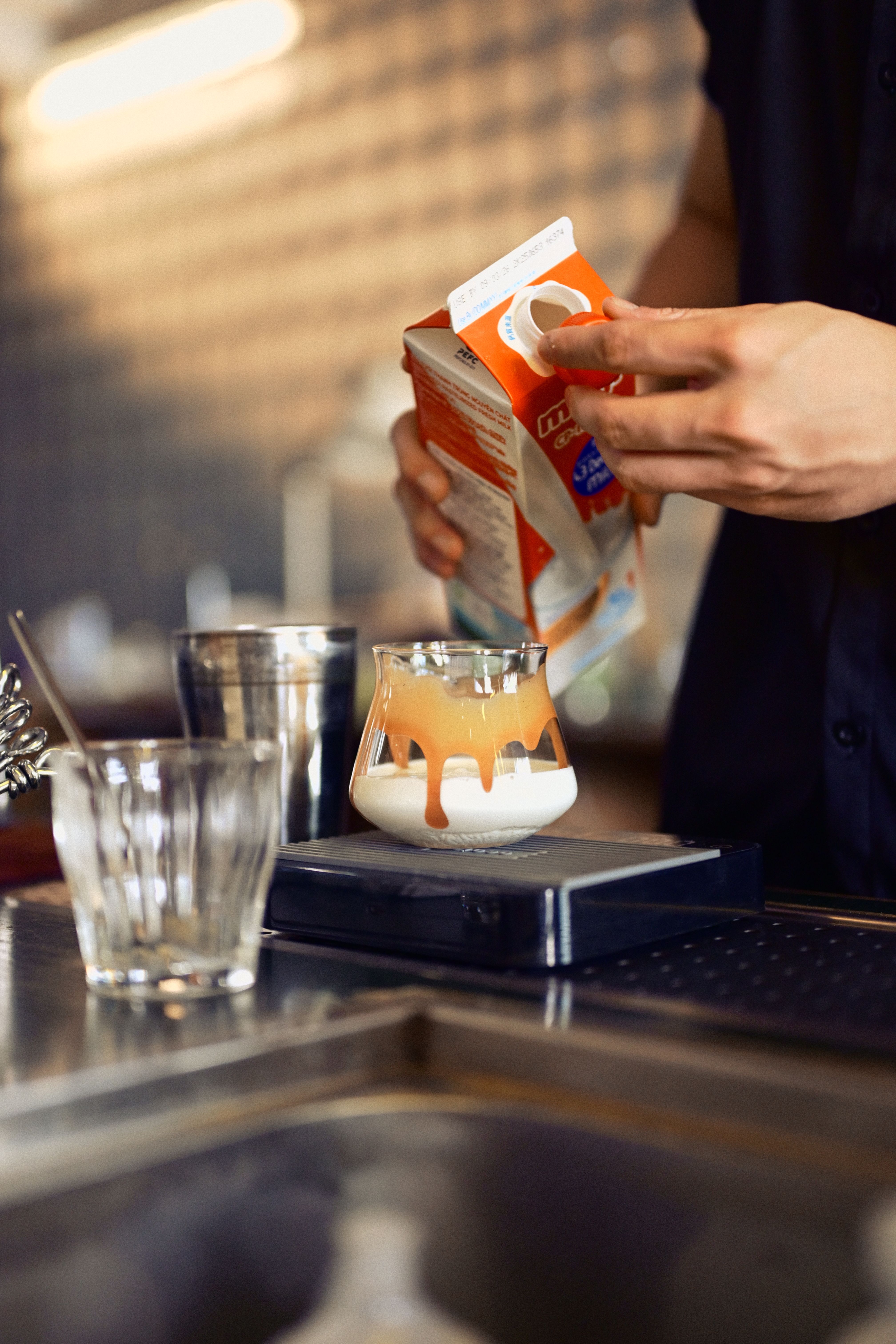 A barista skillfully pours milk into a glass, preparing a creamy coffee in a modern café setting.