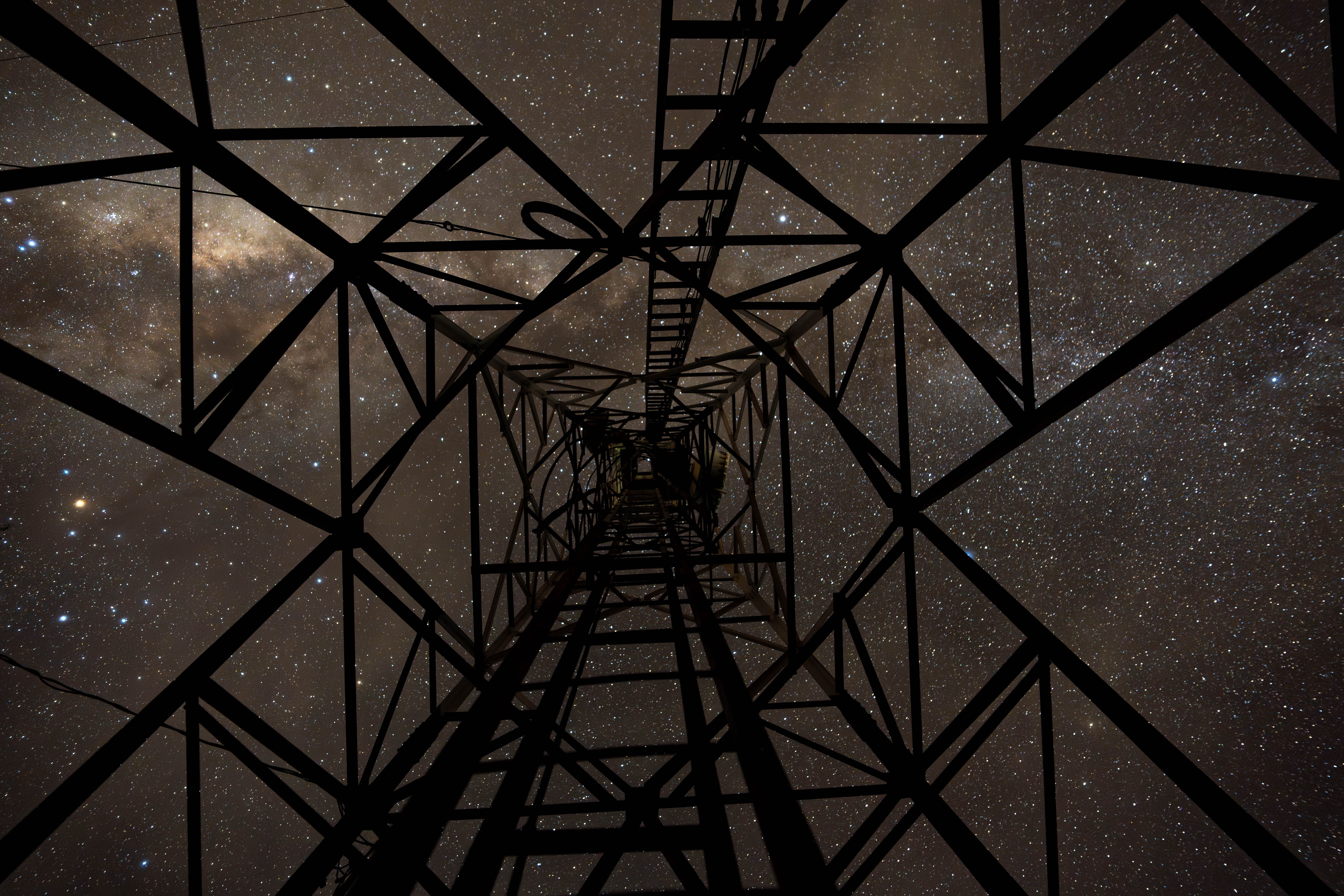 View of the starry night sky through the geometric frame of a metal tower under the Milky Way.