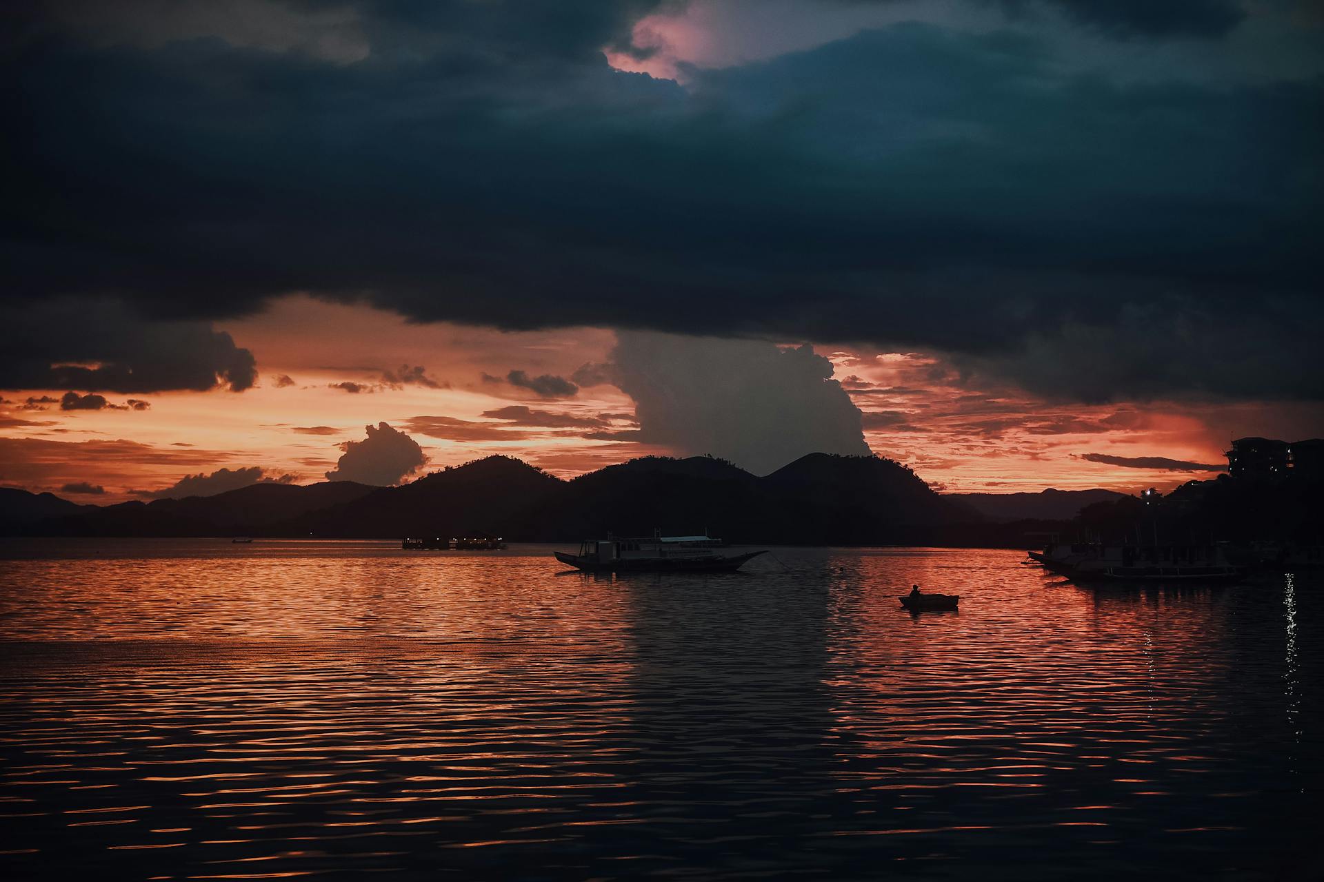 Beautiful sunset over a tranquil lake with silhouetted boats and hills.