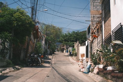 Free A quiet residential street under the sun featuring parked motorcycles and lush greenery. Stock Photo
