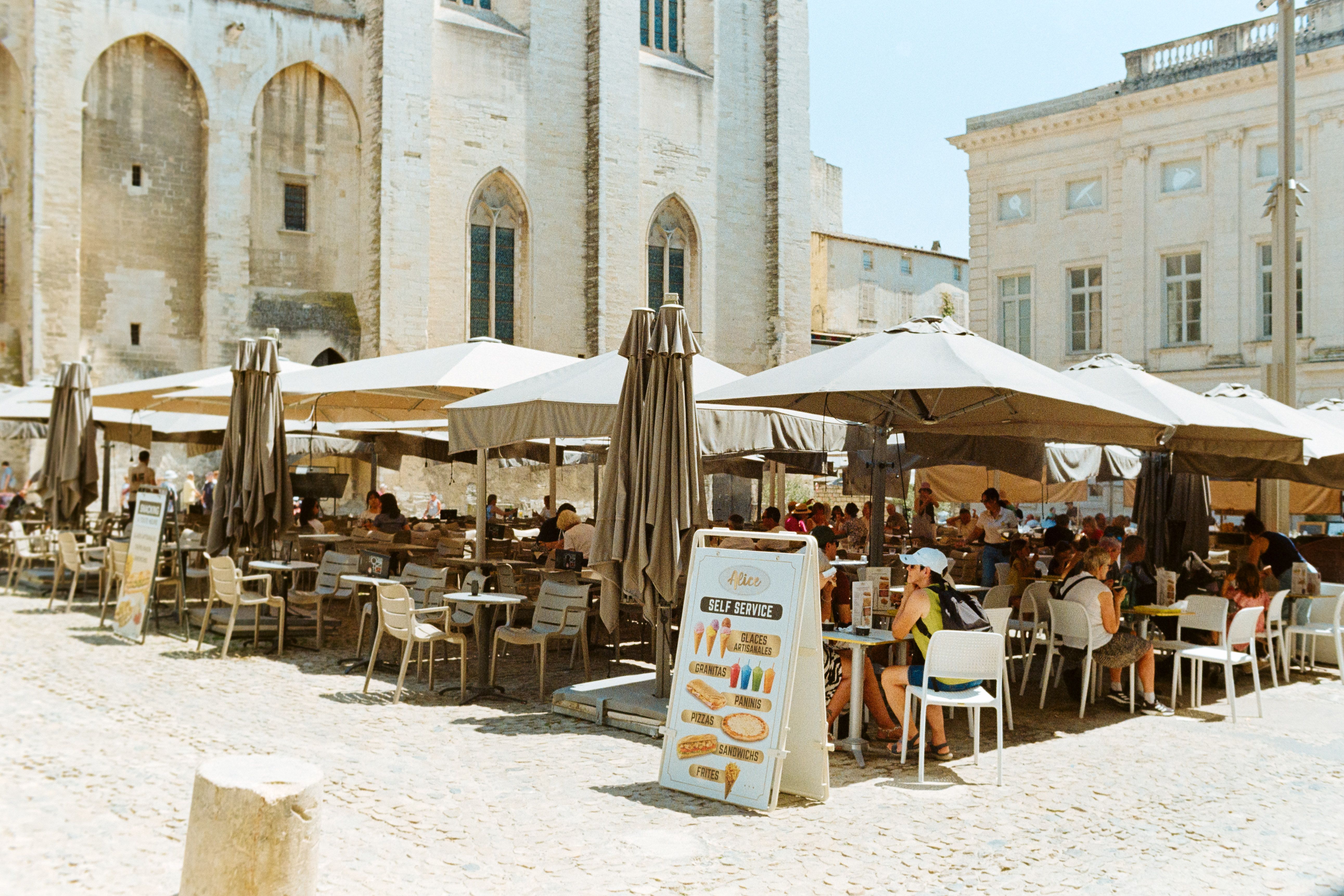 Gäste speisen unter Sonnenschirmen in einem belebten Straßencafé in Avignon