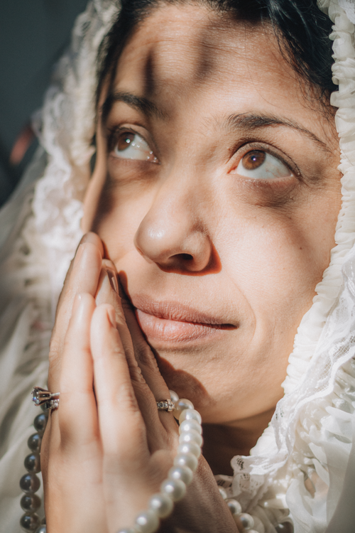 Free Woman in white veil praying with clasped hands and rosary in sunlight. Stock Photo