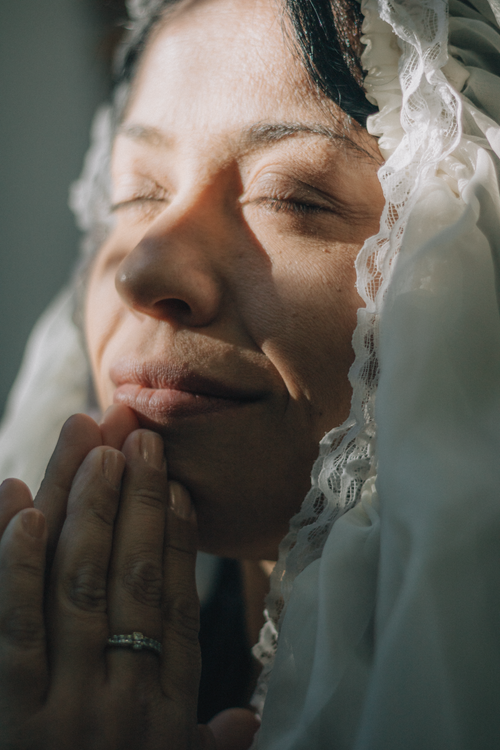 Free Close-up of a serene woman praying, eyes closed, in sunlight with lace veil. Stock Photo