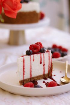 A close-up of a cheesecake slice topped with fresh berries and syrup on a plate.