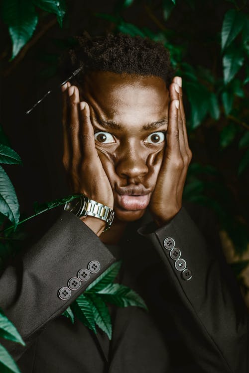 Funny black man making grimace while standing against green tree